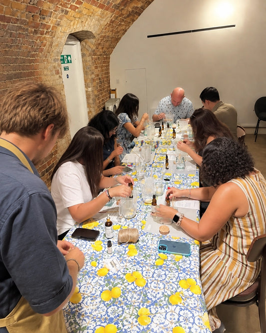A team gathered around a candle-making workshop table in London, heads down over their own candles