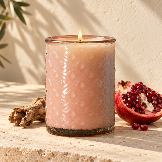 Ischia blush glass candle with pomegranate and wood on a pale stone surface
